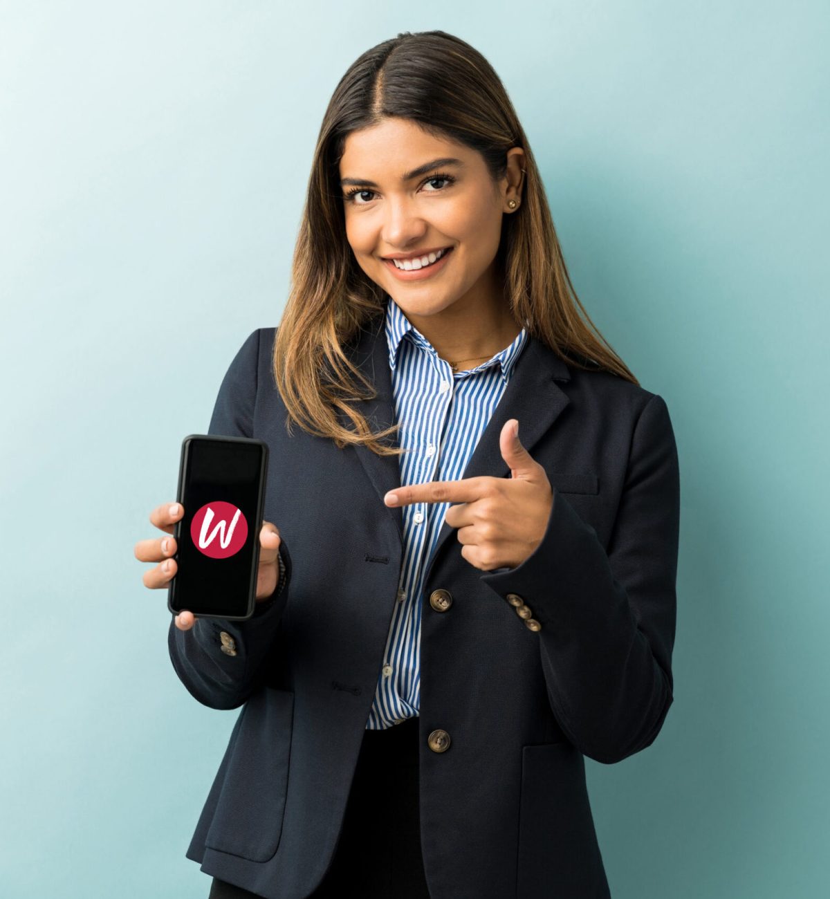 Good looking young female executive pointing at mobile phone while standing at studio